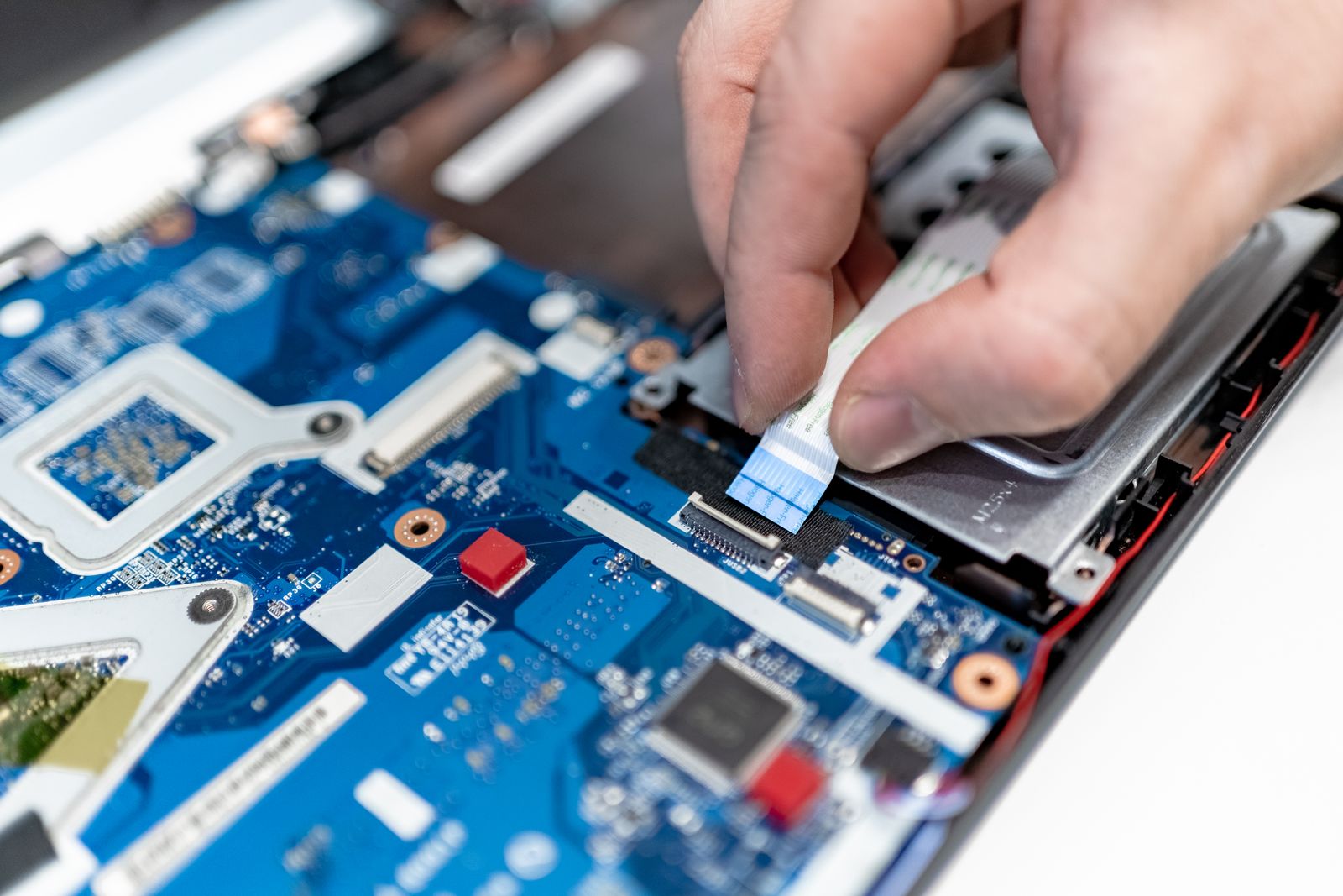 Conserto de notebook: técnico encaixando o cabo flat na placa de um notebook aberto